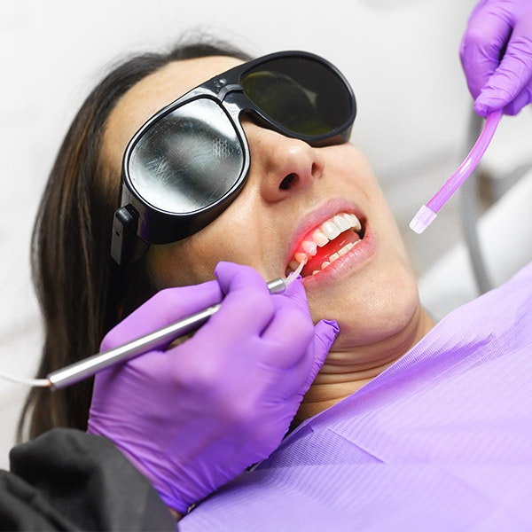 A patient undergoing laser gum surgery (LANAP) with a periodontist using a specialized dental laser and suction tool, while the patient wears protective safety glasses.