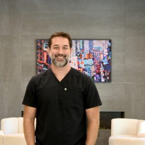 Dr. Thiago Morelli smiling in black scrubs at NC Implants and Periodontics.