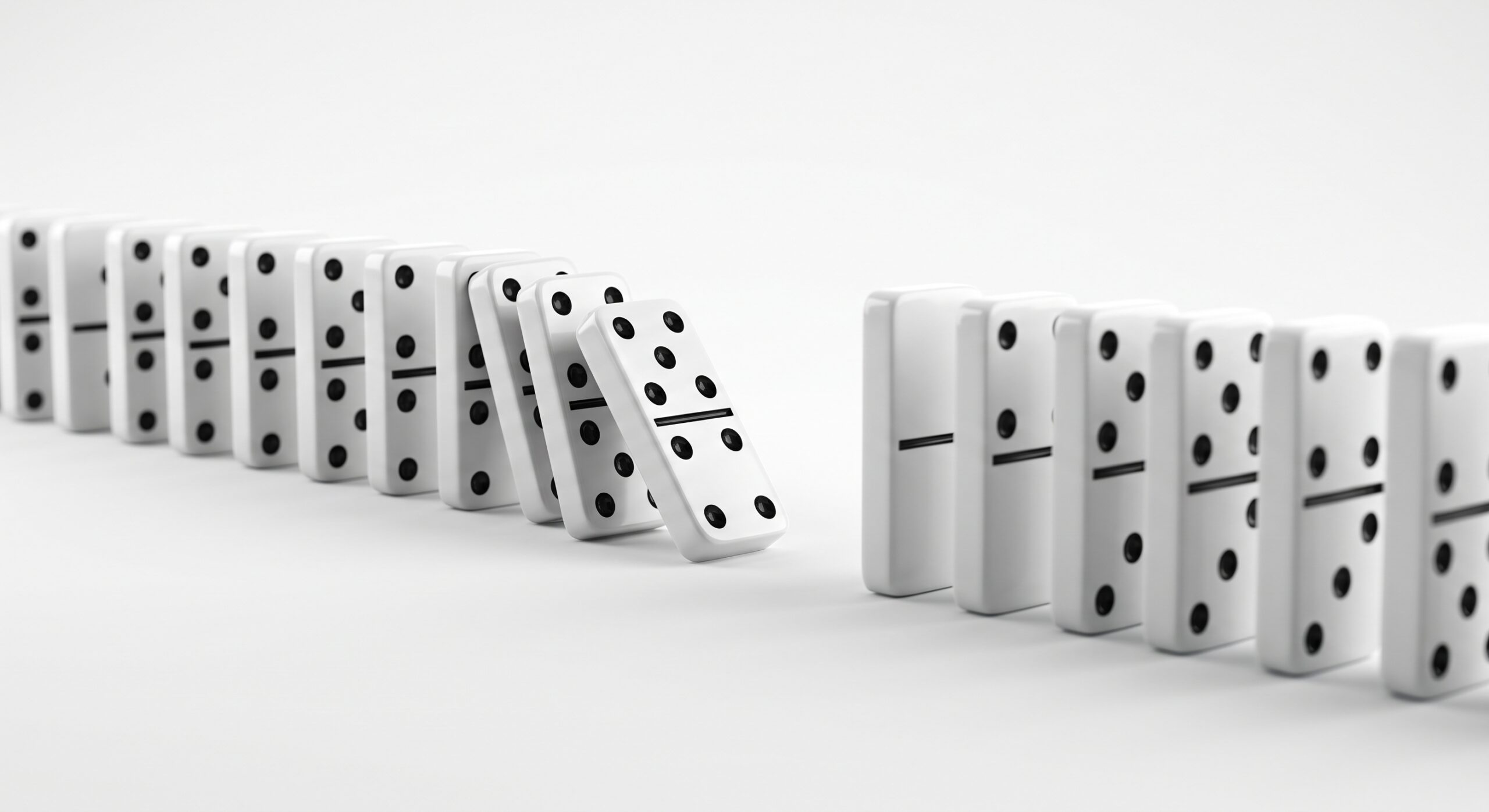 A row of white dominos on a white background with a missing piece in the center, causing the adjacent dominos to tip and fall into the empty gap.